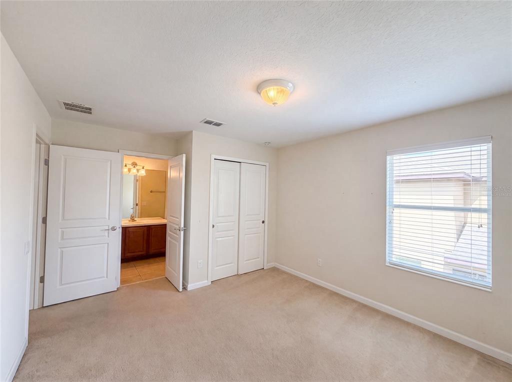 A bedroom with beige carpet, white walls, a closet, and an attached bathroom — 13228 ROSKIN LANE, WINDERMERE, FL