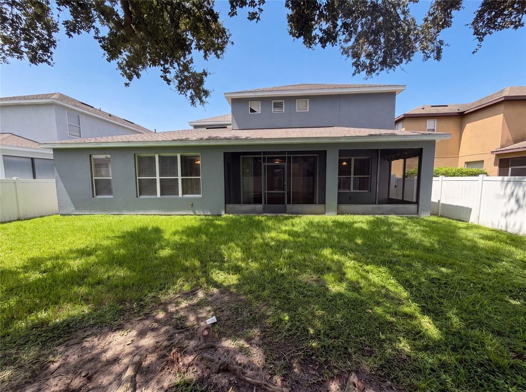 The rear exterior of a two-story gray house features a screened-in patio and fenced yard — 13228 ROSKIN LANE, WINDERMERE, FL