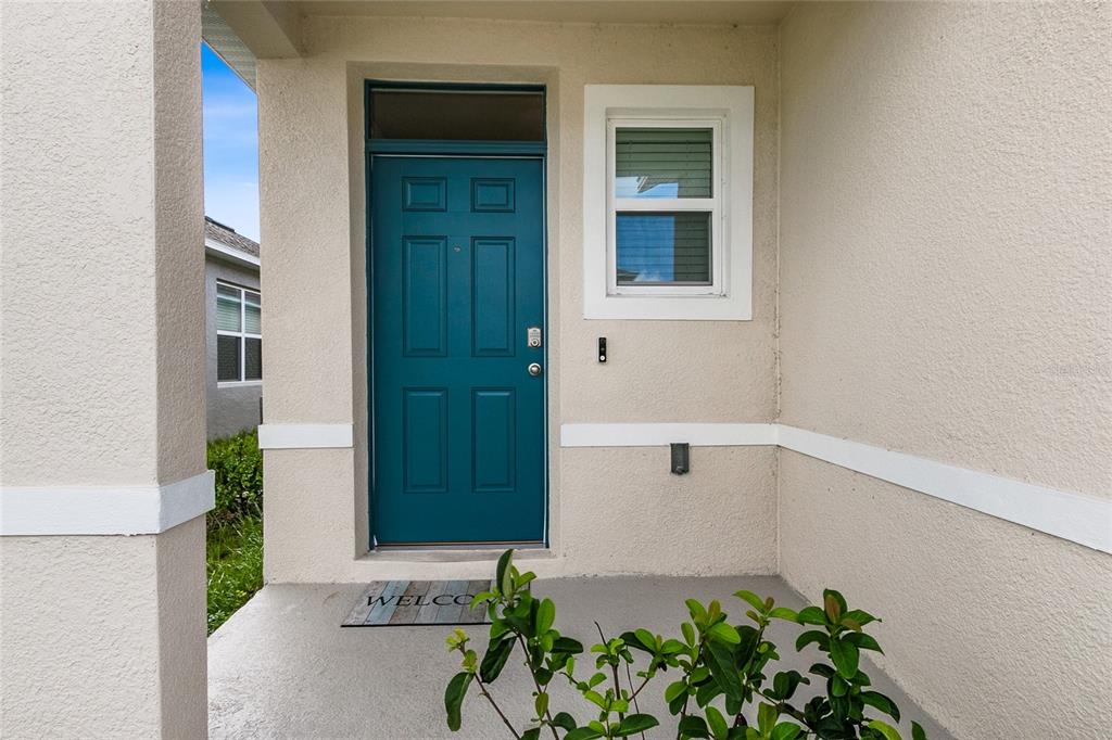 A teal front door with a transom window sits on a covered concrete porch — 3306 PINE LILY AVENUE, POINCIANA, FL
