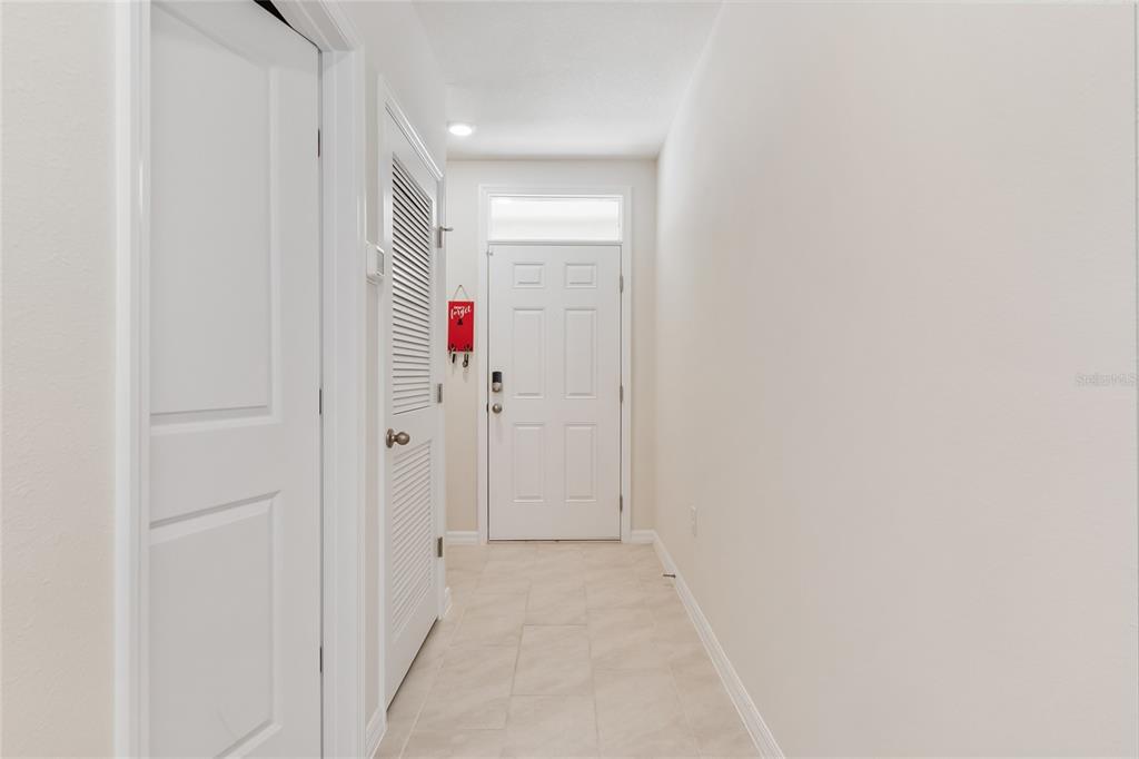 A bright entryway features a white front door, tiled flooring, and two louvered closet doors — 3306 PINE LILY AVENUE, POINCIANA, FL