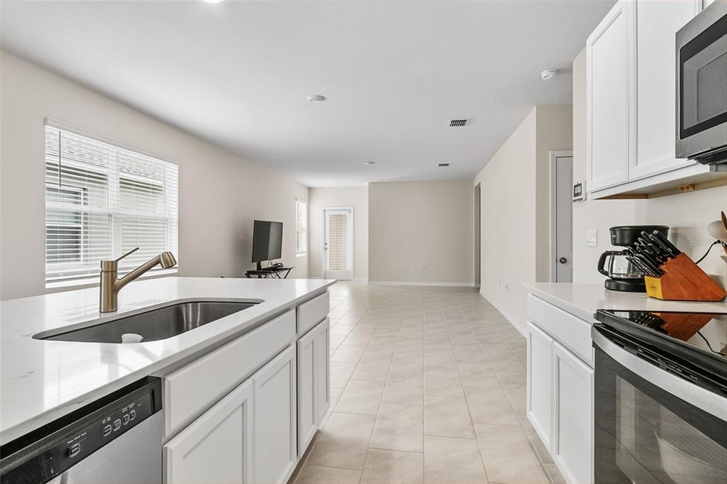 A kitchen with white cabinets and a quartz island overlooks an open-concept living area — 3306 PINE LILY AVENUE, POINCIANA, FL