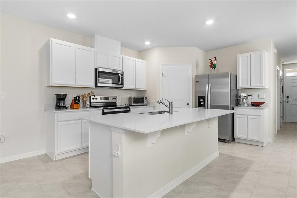 A modern kitchen features white cabinetry, stainless steel appliances, and a large central island — 3306 PINE LILY AVENUE, POINCIANA, FL