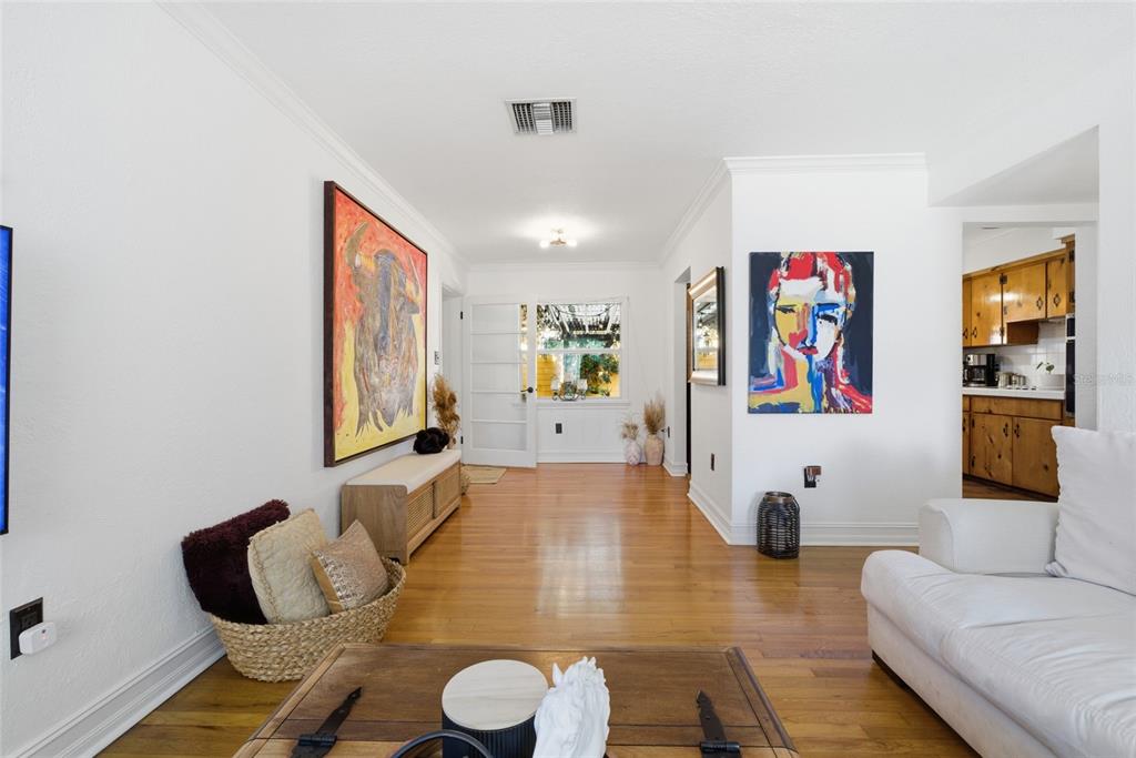 A living room with hardwood floors, white walls, two large paintings, and a kitchen view — 1927 ELAND AVENUE, WINTER PARK, FL