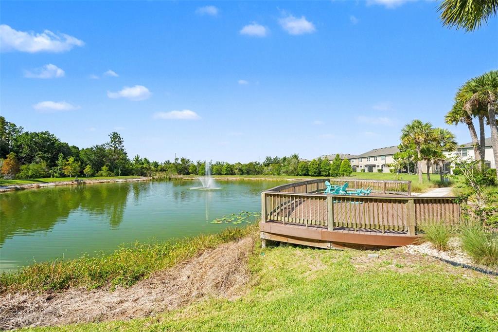 A wooden deck overlooks a pond with a fountain and surrounding trees under a blue sky — 30329 SOUTHWELL LANE, WESLEY CHAPEL, FL