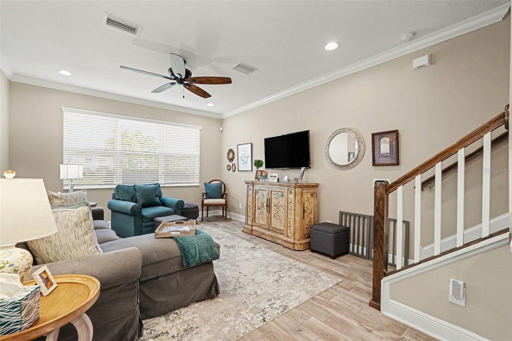 A living room features a grey sectional, a teal armchair, a television, and wooden stairs — 30329 SOUTHWELL LANE, WESLEY CHAPEL, FL
