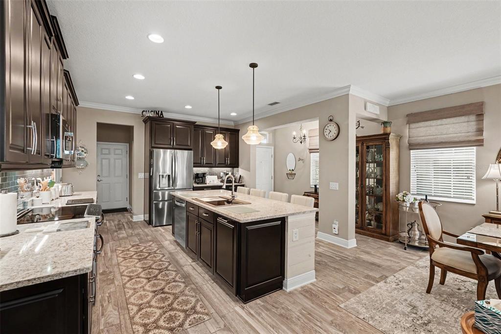 A kitchen features dark wood cabinets, granite countertops, a central island, and light wood flooring — 30329 SOUTHWELL LANE, WESLEY CHAPEL, FL
