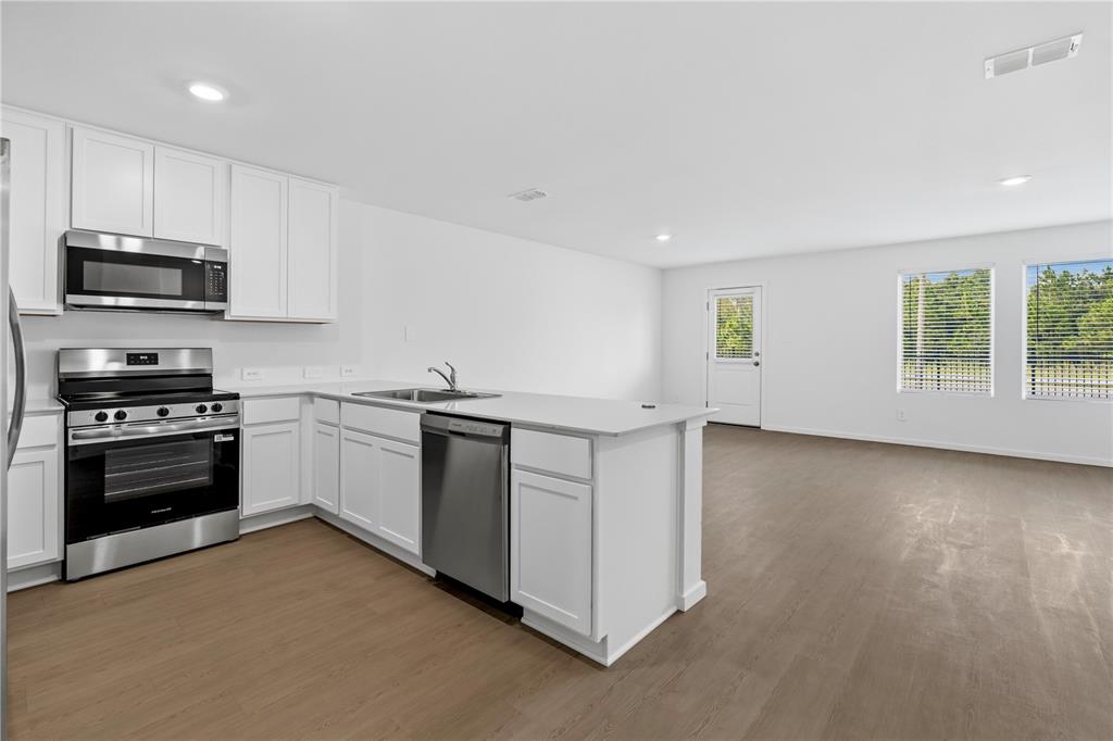 A kitchen with white cabinets, stainless steel appliances, and an island opens to a living area — 1225 ORION STREET, DAVENPORT, FL