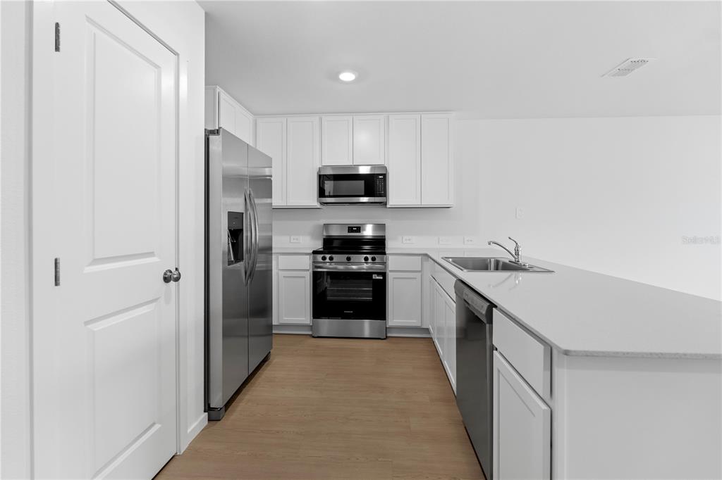 A modern kitchen features white cabinets, stainless steel appliances, and a light-colored countertop island — 1225 ORION STREET, DAVENPORT, FL