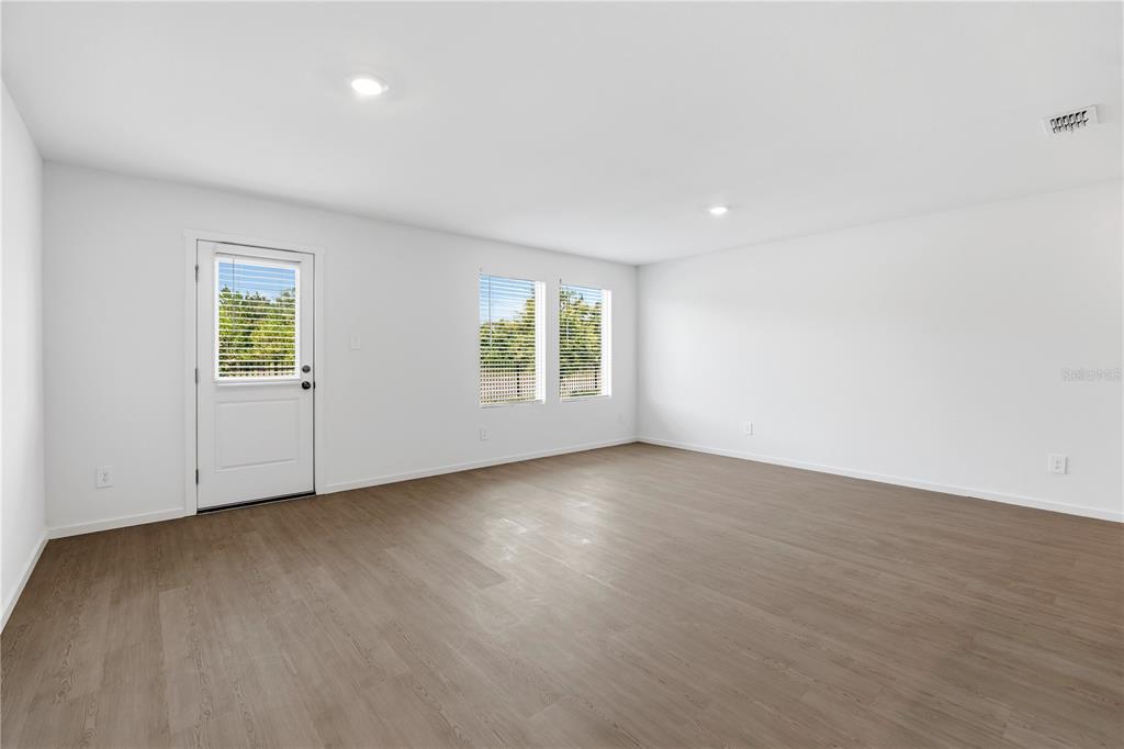 An empty room with white walls, wood-look flooring, two windows, and a white exterior door — 1225 ORION STREET, DAVENPORT, FL