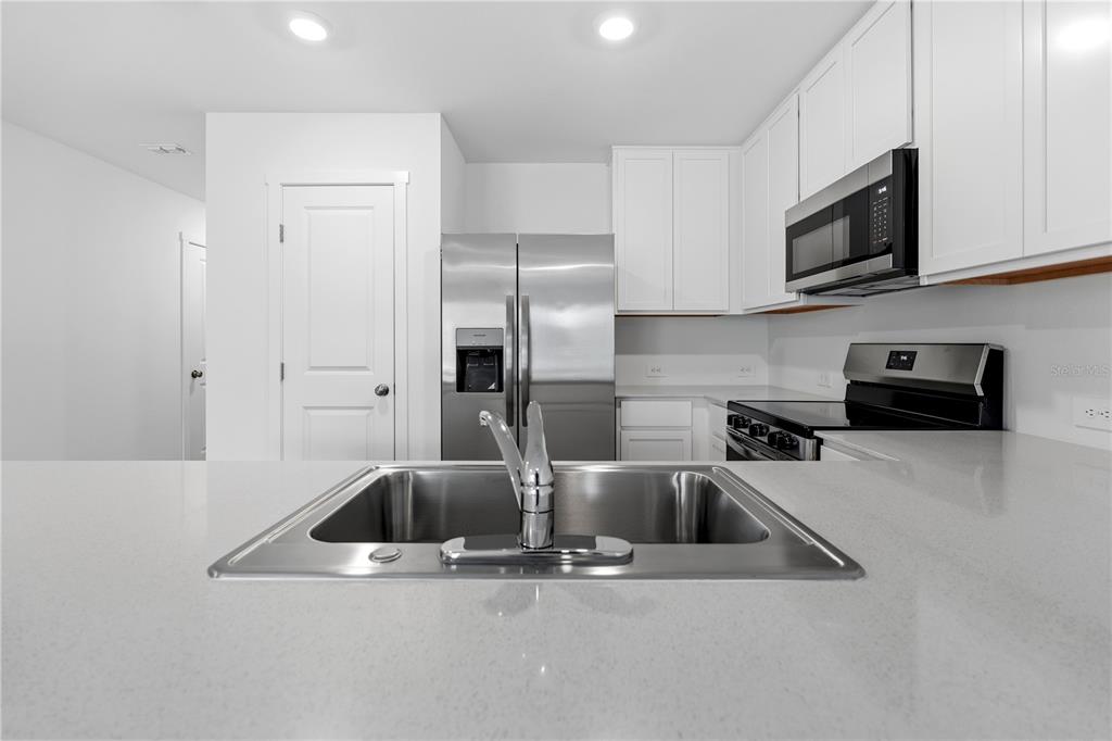A modern kitchen features white cabinets, stainless steel appliances, and a quartz countertop with sink — 1225 ORION STREET, DAVENPORT, FL