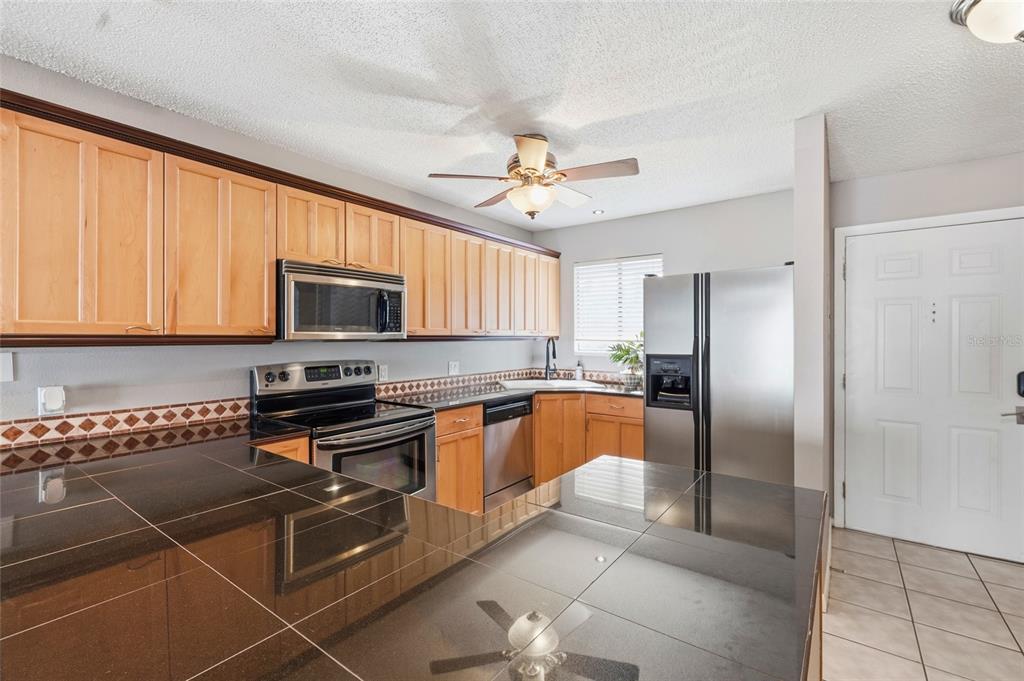 A kitchen features light wood cabinets, black tile countertops, and stainless steel appliances — 6033 34TH STREET W UNIT 80, BRADENTON, FL