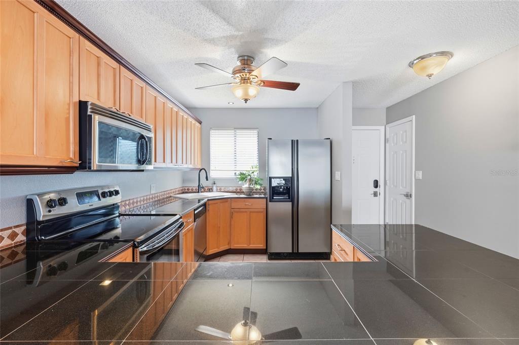 A kitchen features light wood cabinets, black countertops, stainless steel appliances, and a ceiling fan — 6033 34TH STREET W UNIT 80, BRADENTON, FL