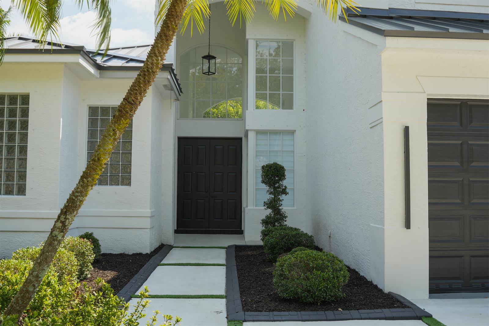 A white house exterior features a dark double front door, glass block windows, and landscaping — 5227 SW 195th Terrace, Miramar FL 33029, MIRAMAR, FL