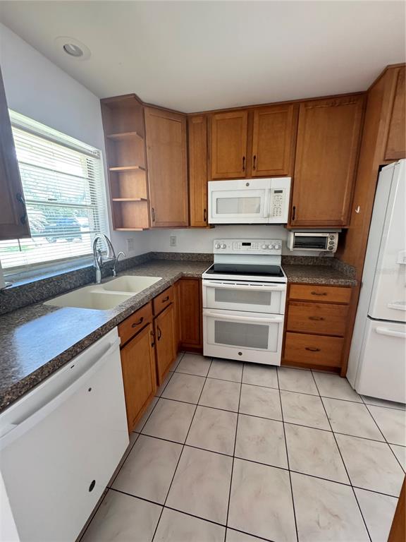 A kitchen features wood cabinets, white appliances, a double sink, and light-colored tile flooring — 427 GREENFIELD ROAD, WINTER HAVEN, FL