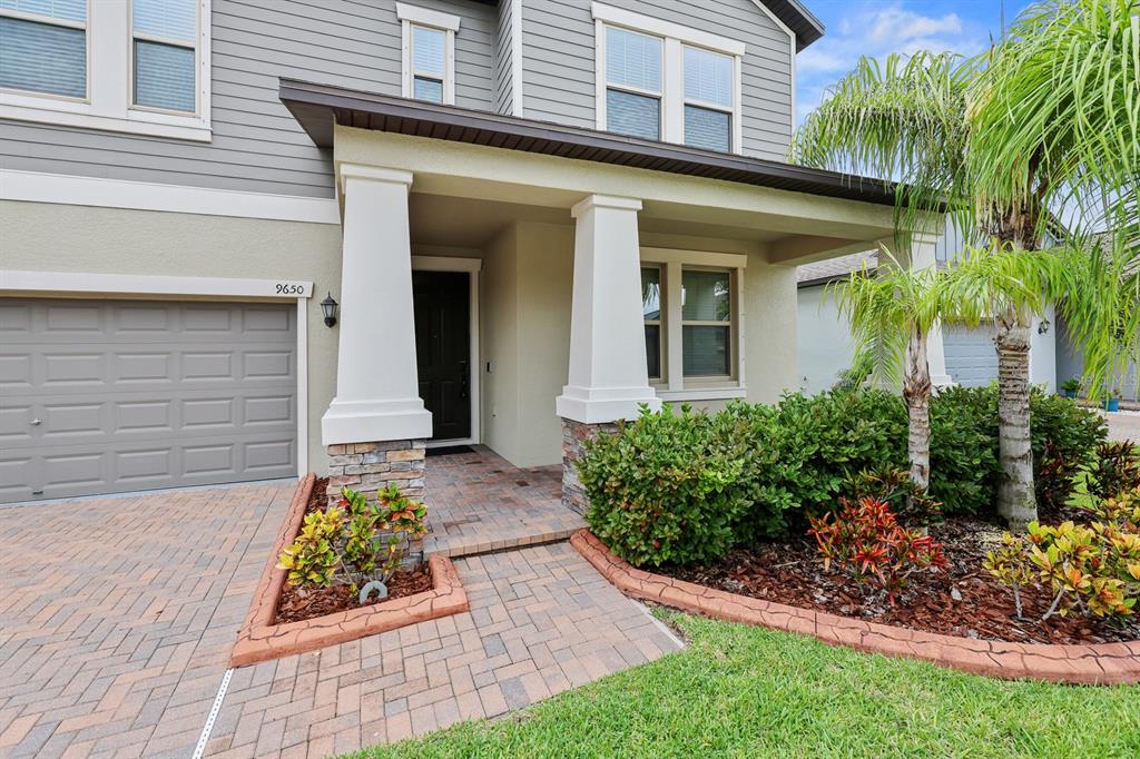 The exterior of a two-story house features a stone-accented porch, a paver driveway, and landscaping — 9650 IVORY DRIVE, RUSKIN, FL