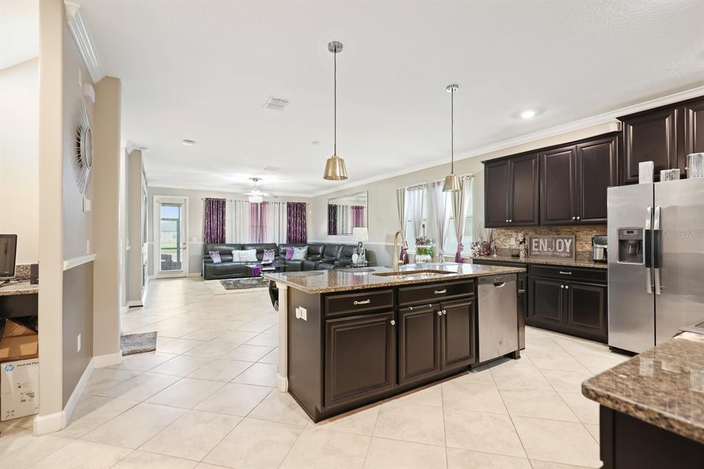 A kitchen with dark cabinets and a granite island opens into a living room area — 9650 IVORY DRIVE, RUSKIN, FL