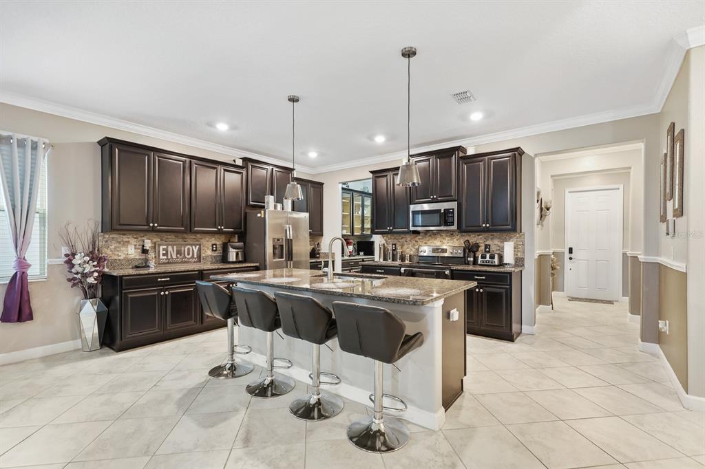A kitchen with dark wood cabinets, granite countertops, a central island, and four bar stools — 9650 IVORY DRIVE, RUSKIN, FL