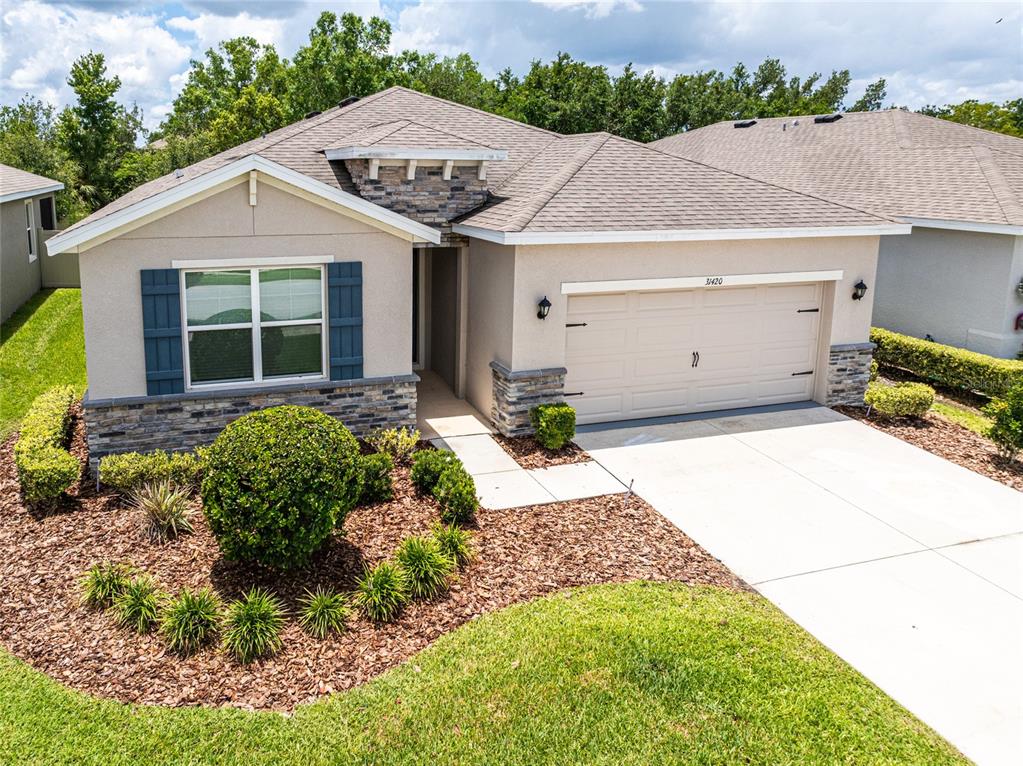 A single-story house with a beige stucco exterior, stone accents, and a two-car garage — 31420 TANSY BEND, WESLEY CHAPEL, FL