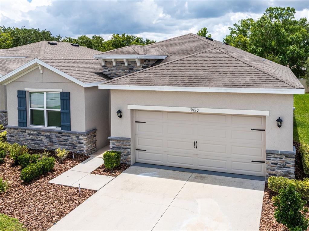 A single-story house exterior features a two-car garage, stone accents, and blue window shutters — 31420 TANSY BEND, WESLEY CHAPEL, FL