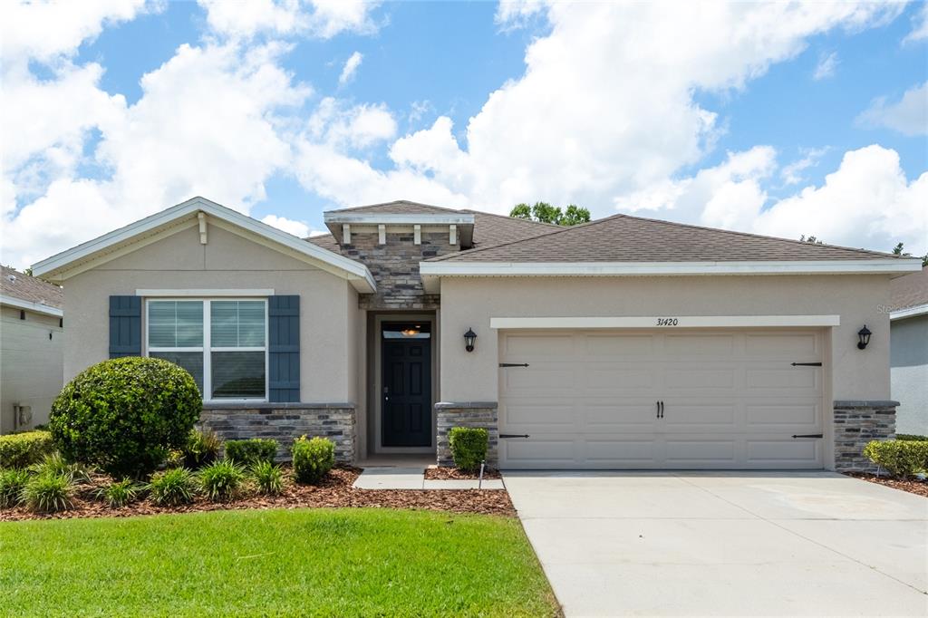 A single-story house with a beige stucco exterior, stone accents, and a two-car garage — 31420 TANSY BEND, WESLEY CHAPEL, FL