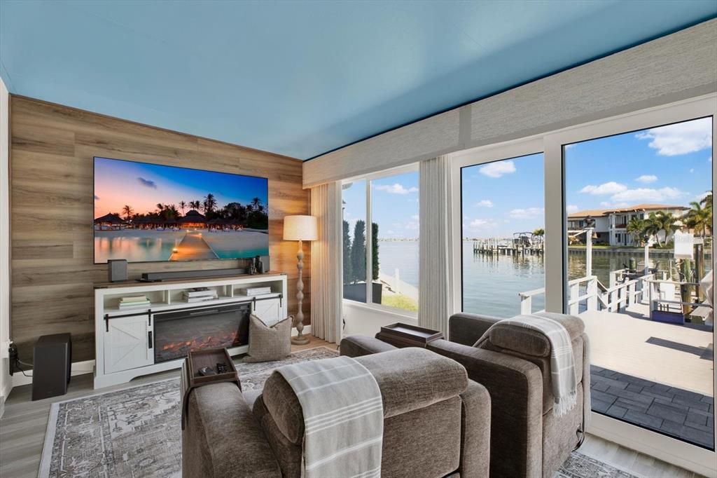 A living room features a wood-paneled wall, a fireplace console, and floor-to-ceiling waterfront views — 645 BOCA CIEGA POINT BOULEVARD N, ST PETERSBURG, FL