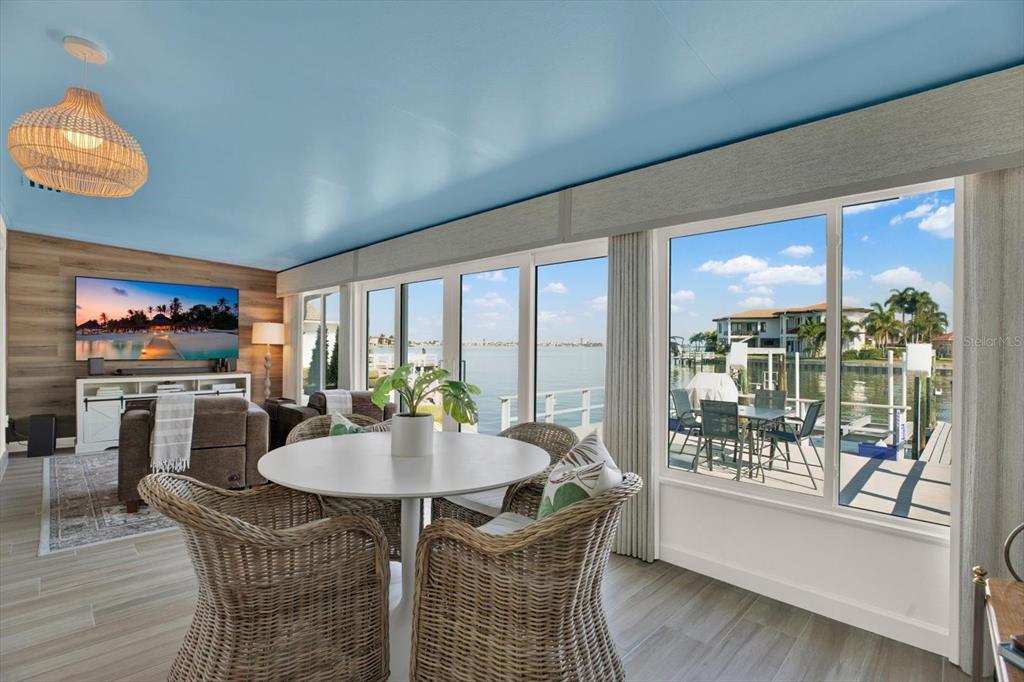A dining area with wicker chairs overlooks a waterfront patio through large glass doors — 645 BOCA CIEGA POINT BOULEVARD N, ST PETERSBURG, FL