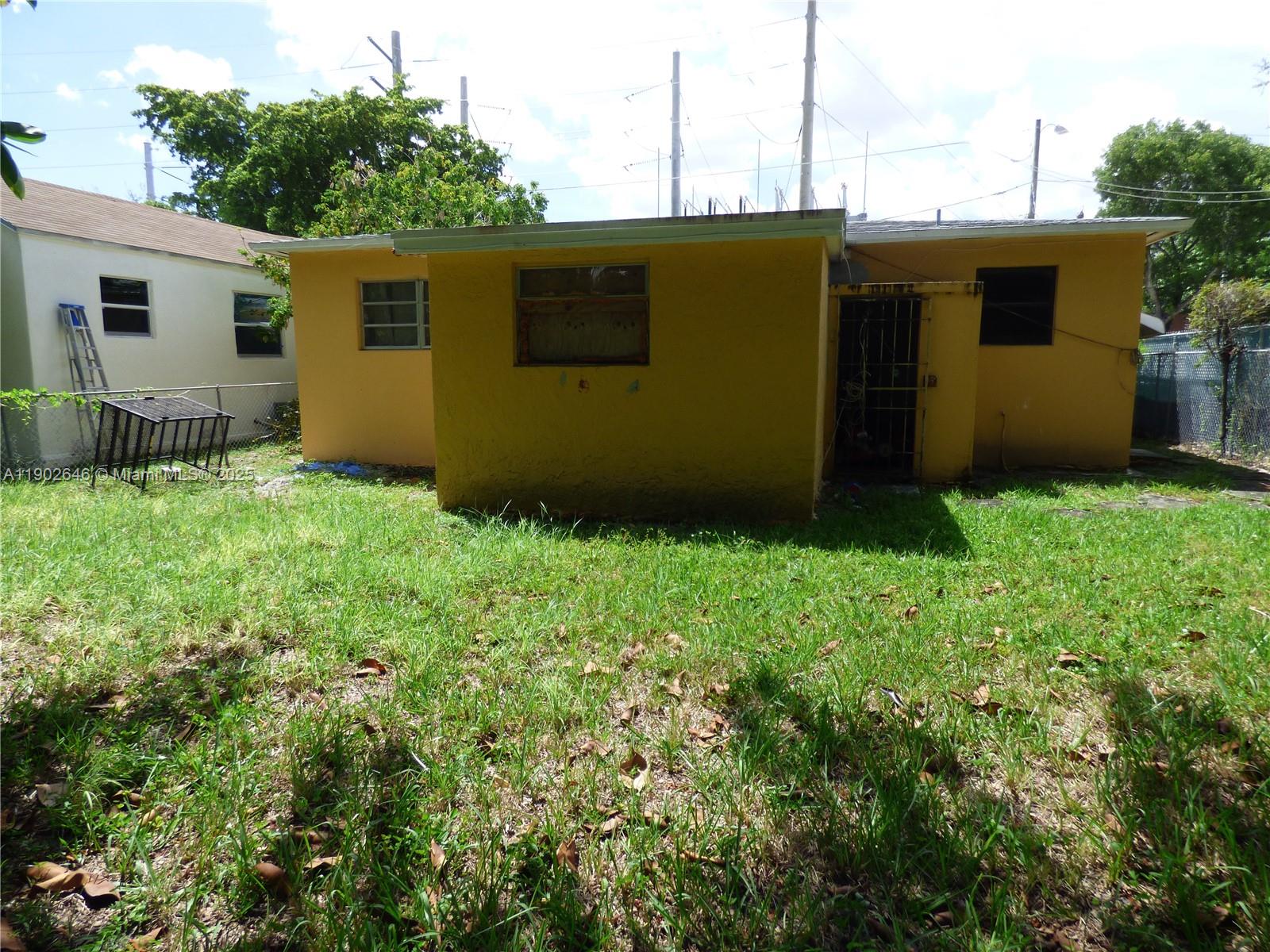 The exterior of a yellow house features a small backyard and a metal security gate — 347 NW 42nd St, Miami FL 33127, MIAMI, FL
