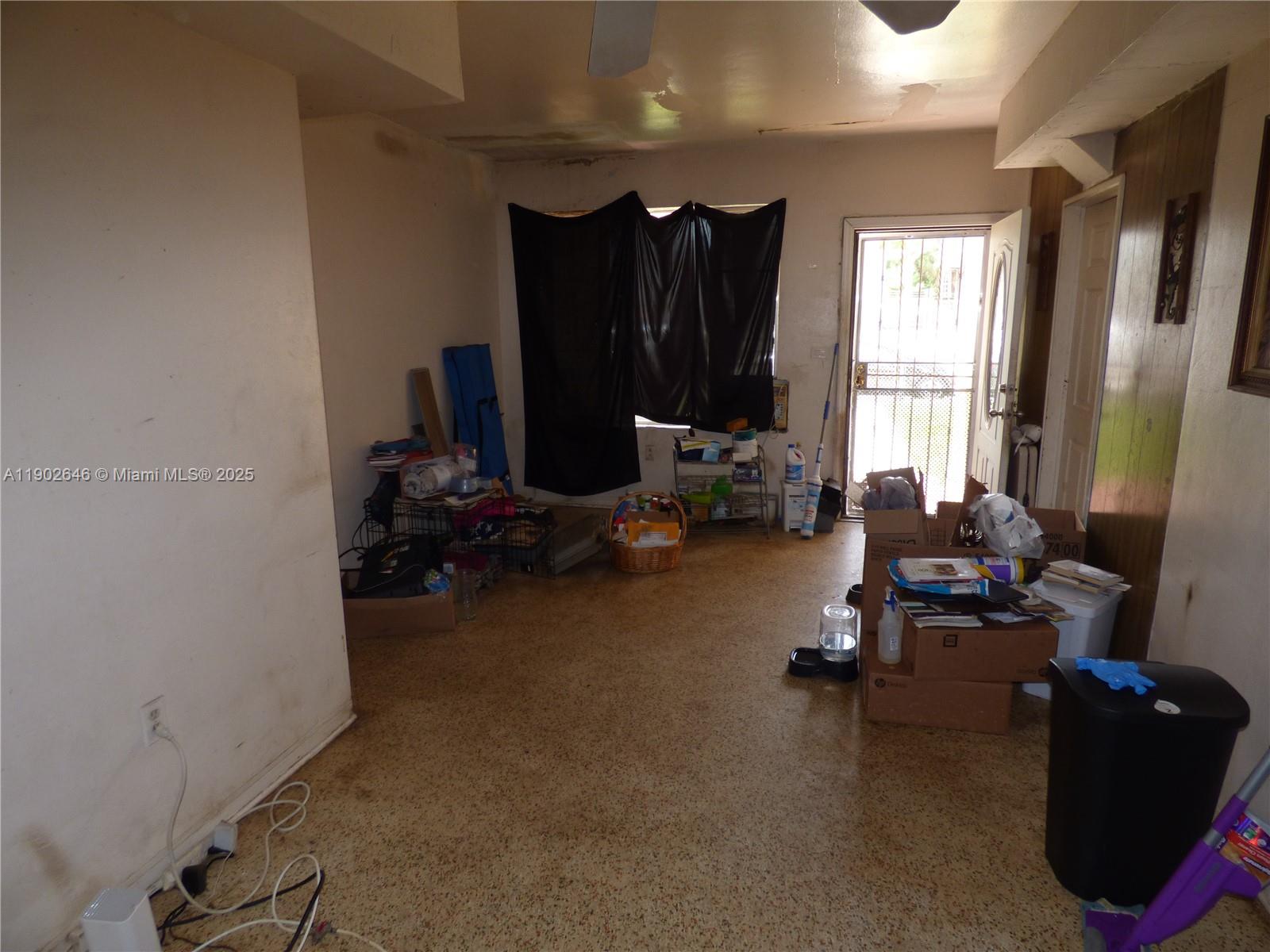 A cluttered room features a terrazzo floor, a window with black curtains, and an exterior door — 347 NW 42nd St, Miami FL 33127, MIAMI, FL