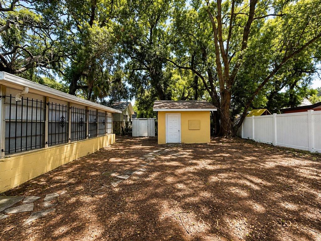 A backyard features a yellow shed, a white fence, and a house with barred windows — 1003 E 22ND AVENUE, TAMPA, FL