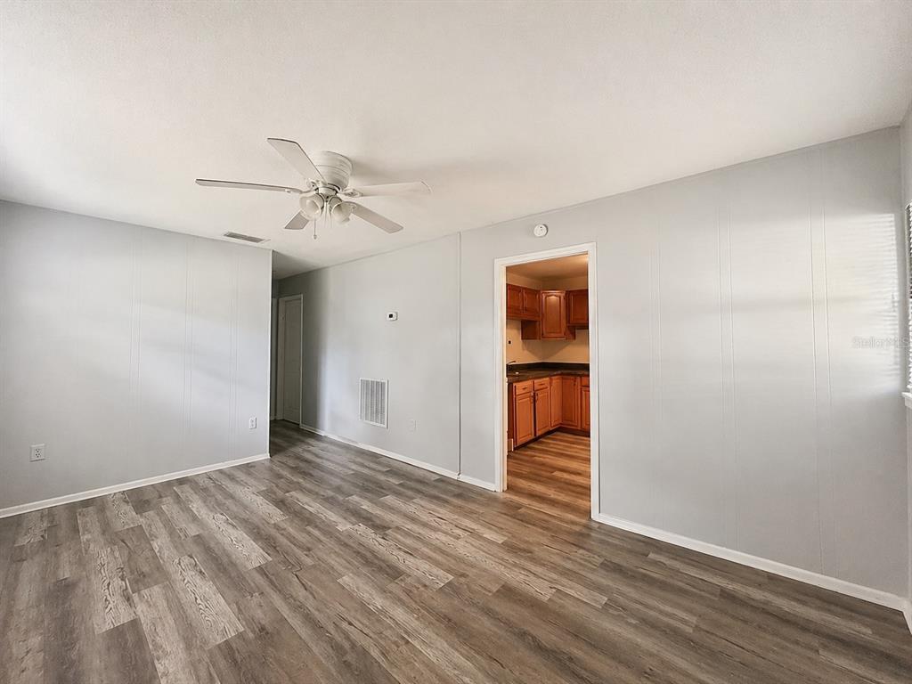A living room with light gray walls, wood-look flooring, and a ceiling fan leads to a kitchen — 1003 E 22ND AVENUE, TAMPA, FL
