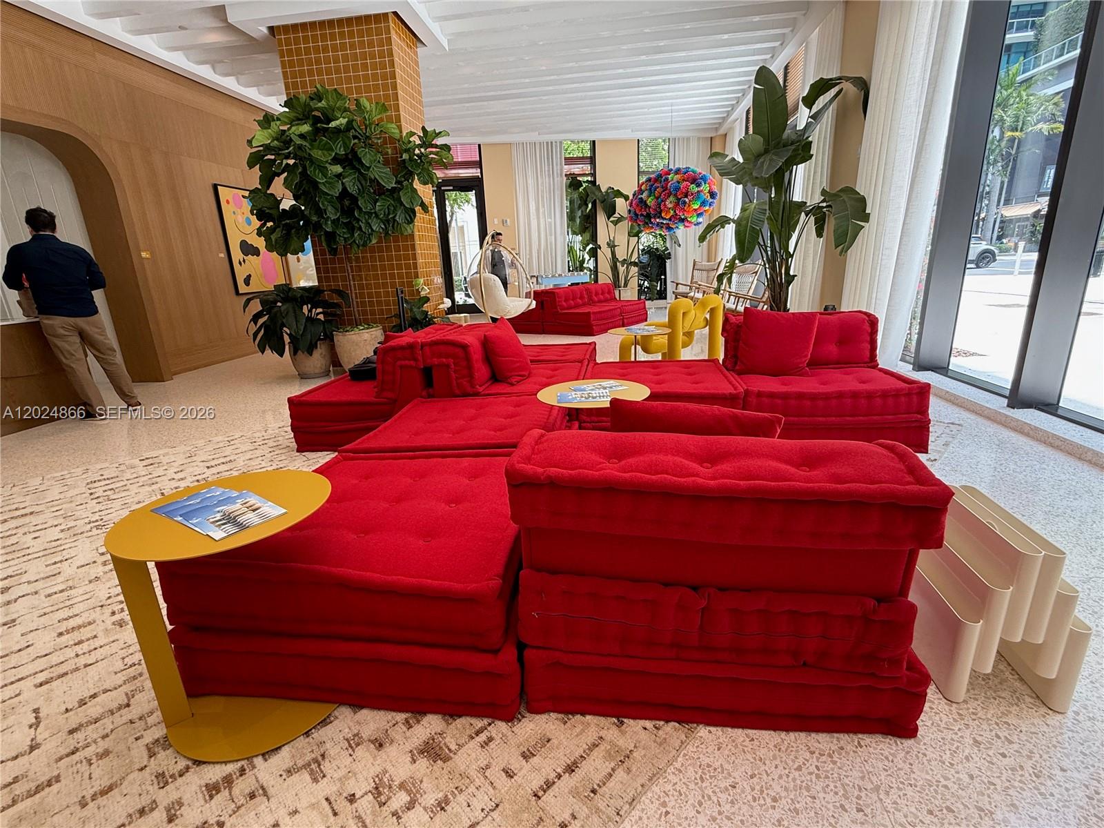 A modern lobby features modular red seating, yellow accent tables, and large potted plants — 90 NE 32 # 412, Miami FL 33137, MIAMI, FL