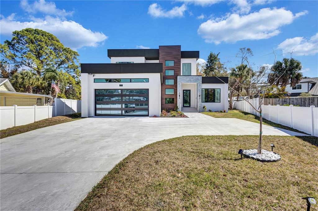 A modern two-story house features a glass garage door, wood-paneled accent wall, and concrete driveway — 275 LIME CIRCLE, SARASOTA, FL