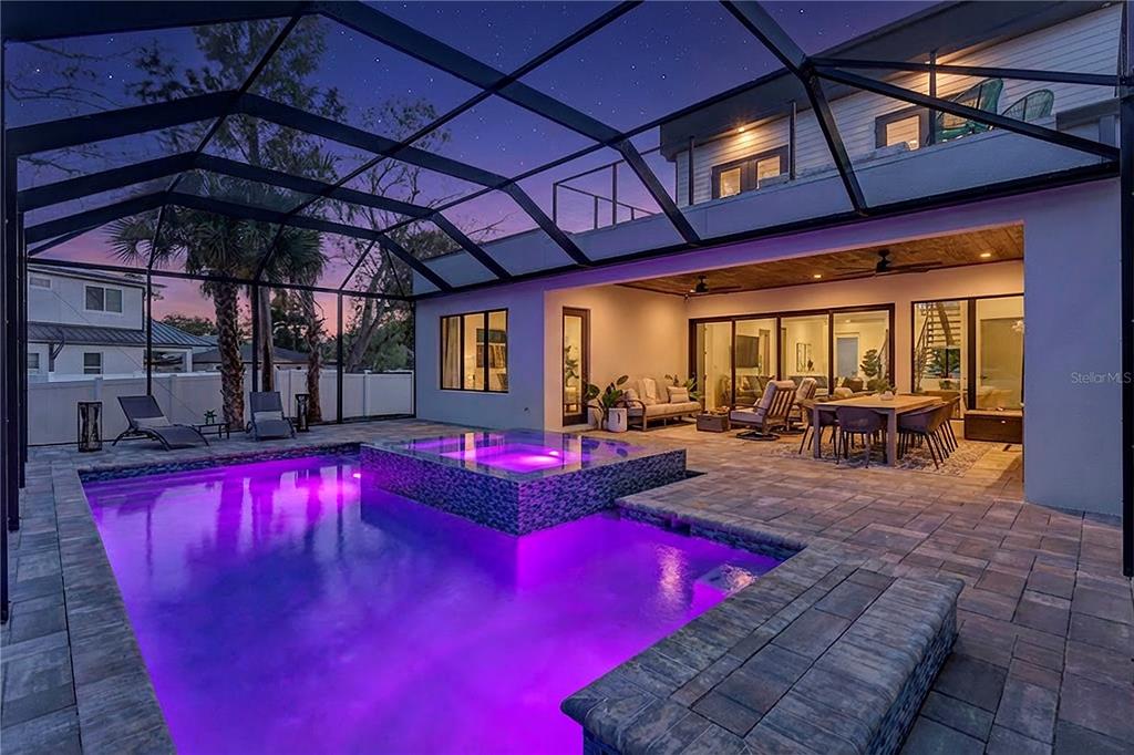 A screened-in patio features a purple-lit swimming pool with an integrated hot tub at dusk — 275 LIME CIRCLE, SARASOTA, FL