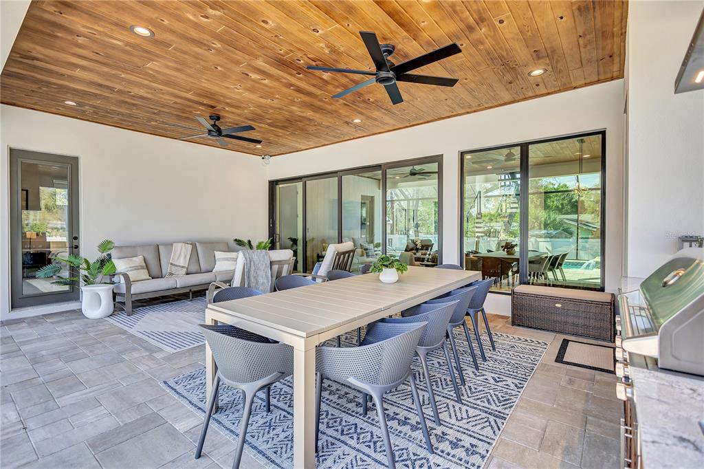 A covered outdoor patio features a wood-paneled ceiling, dining area, and sliding glass doors — 275 LIME CIRCLE, SARASOTA, FL