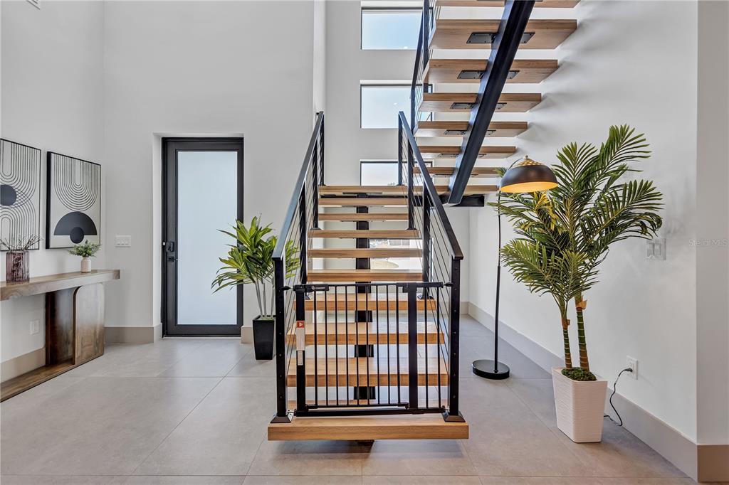 A modern entryway features a floating wooden staircase with a black metal safety gate — 275 LIME CIRCLE, SARASOTA, FL