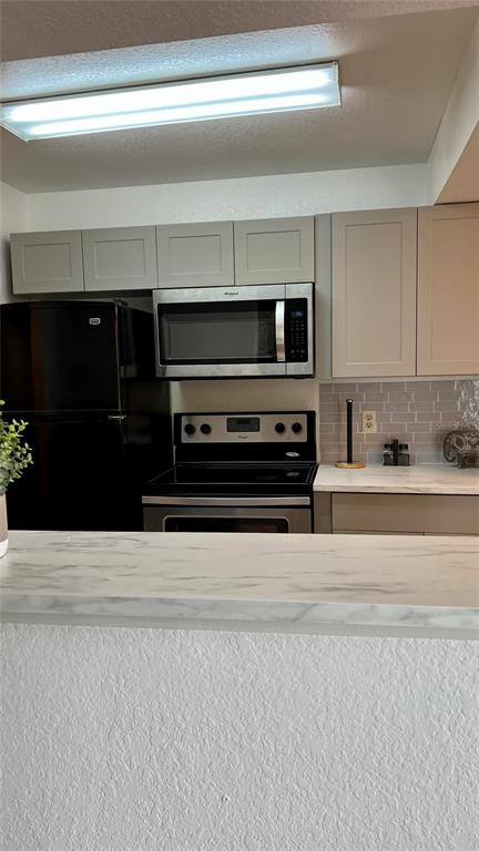 A kitchen features light-colored cabinets, a black refrigerator, a microwave, and a marble-patterned countertop — 11526 WESTWOOD BOULEVARD UNIT 723, ORLANDO, FL