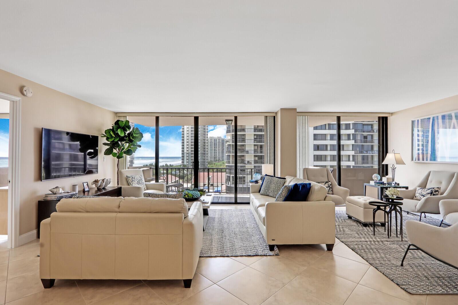 A spacious living room features light-colored sofas, tiled floors, and floor-to-ceiling windows with ocean views — 4200 N Ocean Drive # 802, Singer Island FL 33404, SINGER ISLAND, FL