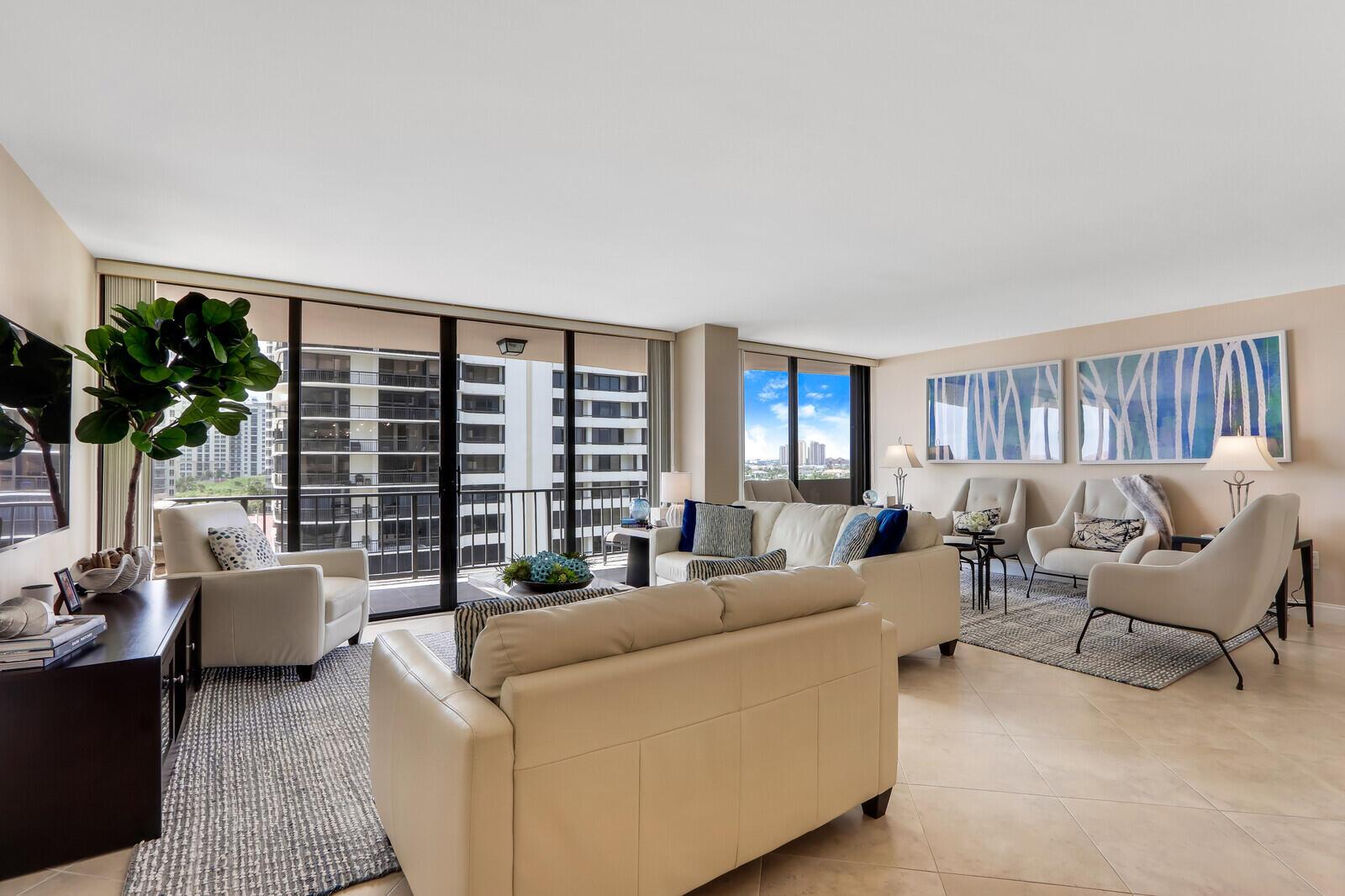 A bright living room features cream leather sofas, armchairs, tile floors, and floor-to-ceiling windows — 4200 N Ocean Drive # 802, Singer Island FL 33404, SINGER ISLAND, FL