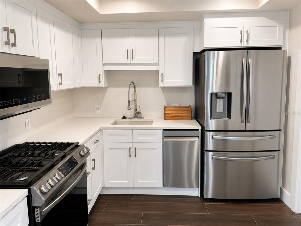 A kitchen features white cabinets, stainless steel appliances, a sink, and dark wood flooring — 1847 SHORE DRIVE S UNIT 101, ST PETERSBURG, FL