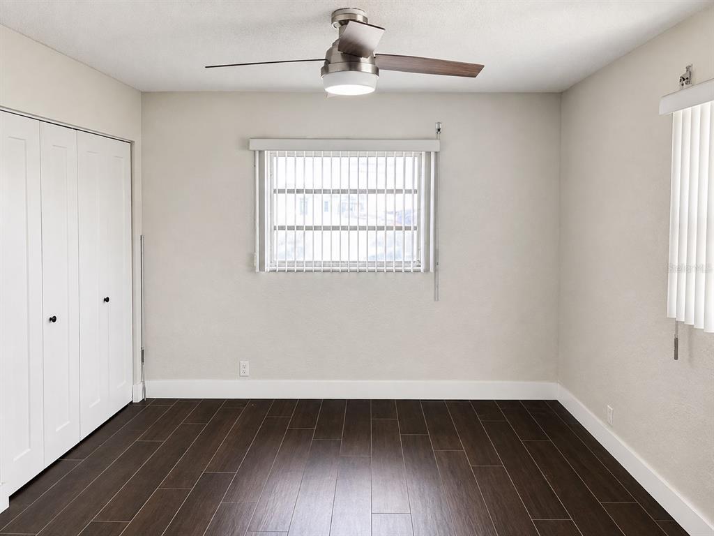 An empty bedroom features dark wood-look flooring, white walls, a ceiling fan, and a window — 1847 SHORE DRIVE S UNIT 101, ST PETERSBURG, FL