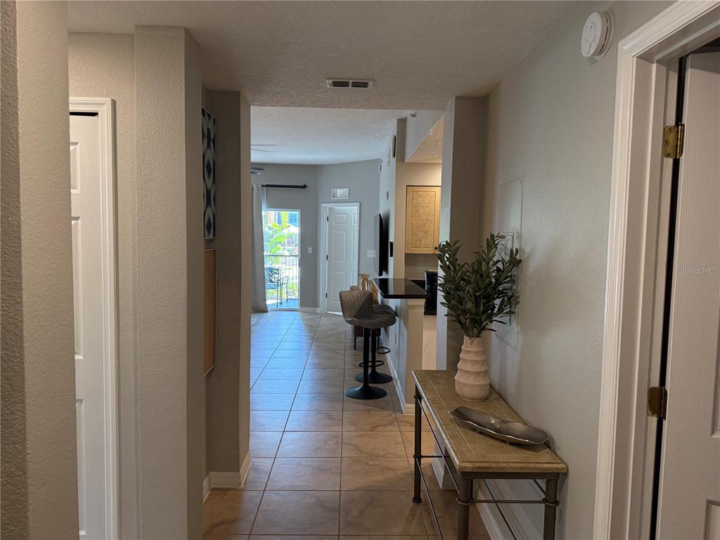 A tiled hallway leads past a console table and breakfast bar toward a balcony door — 8601 WORLDQUEST BOULEVARD UNIT 3105, ORLANDO, FL