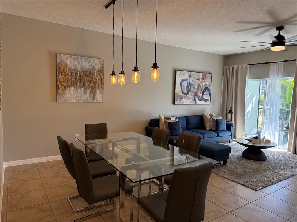 A dining area with a glass table and pendant lights opens into a living room — 8601 WORLDQUEST BOULEVARD UNIT 3105, ORLANDO, FL