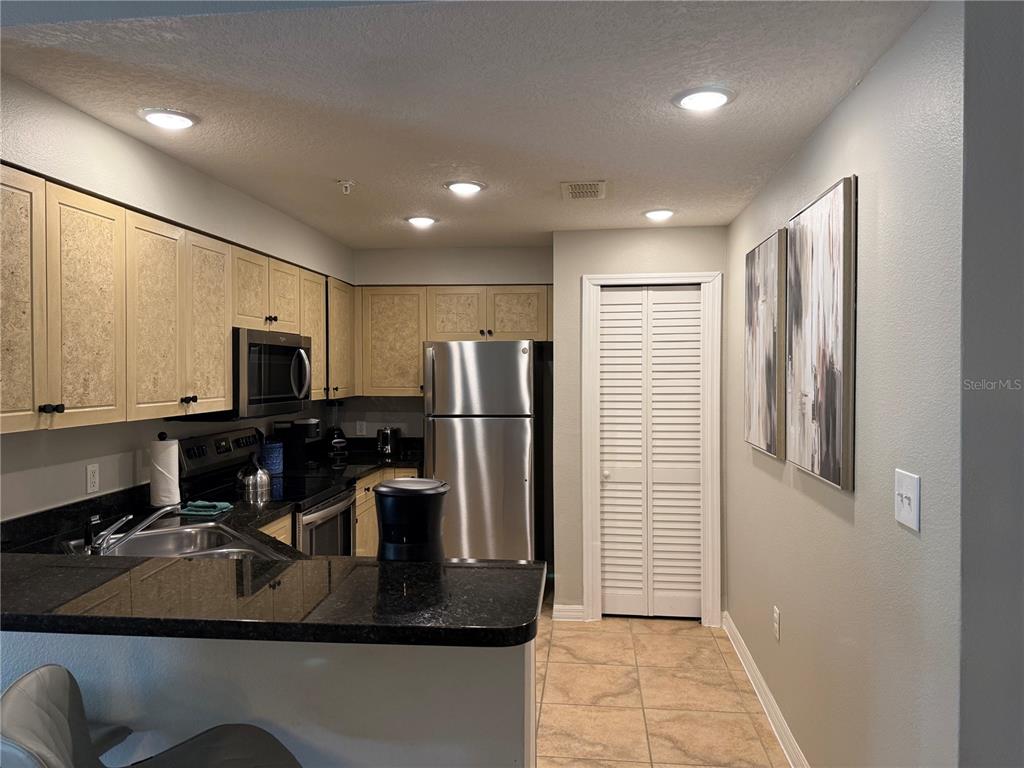 A kitchen features light-colored cabinets, black countertops, stainless steel appliances, and tile flooring — 8601 WORLDQUEST BOULEVARD UNIT 3105, ORLANDO, FL