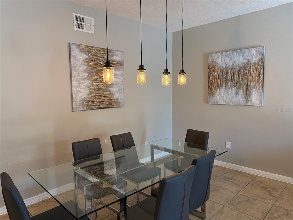 A dining room features a glass table, six dark chairs, and four pendant lights — 8601 WORLDQUEST BOULEVARD UNIT 3105, ORLANDO, FL