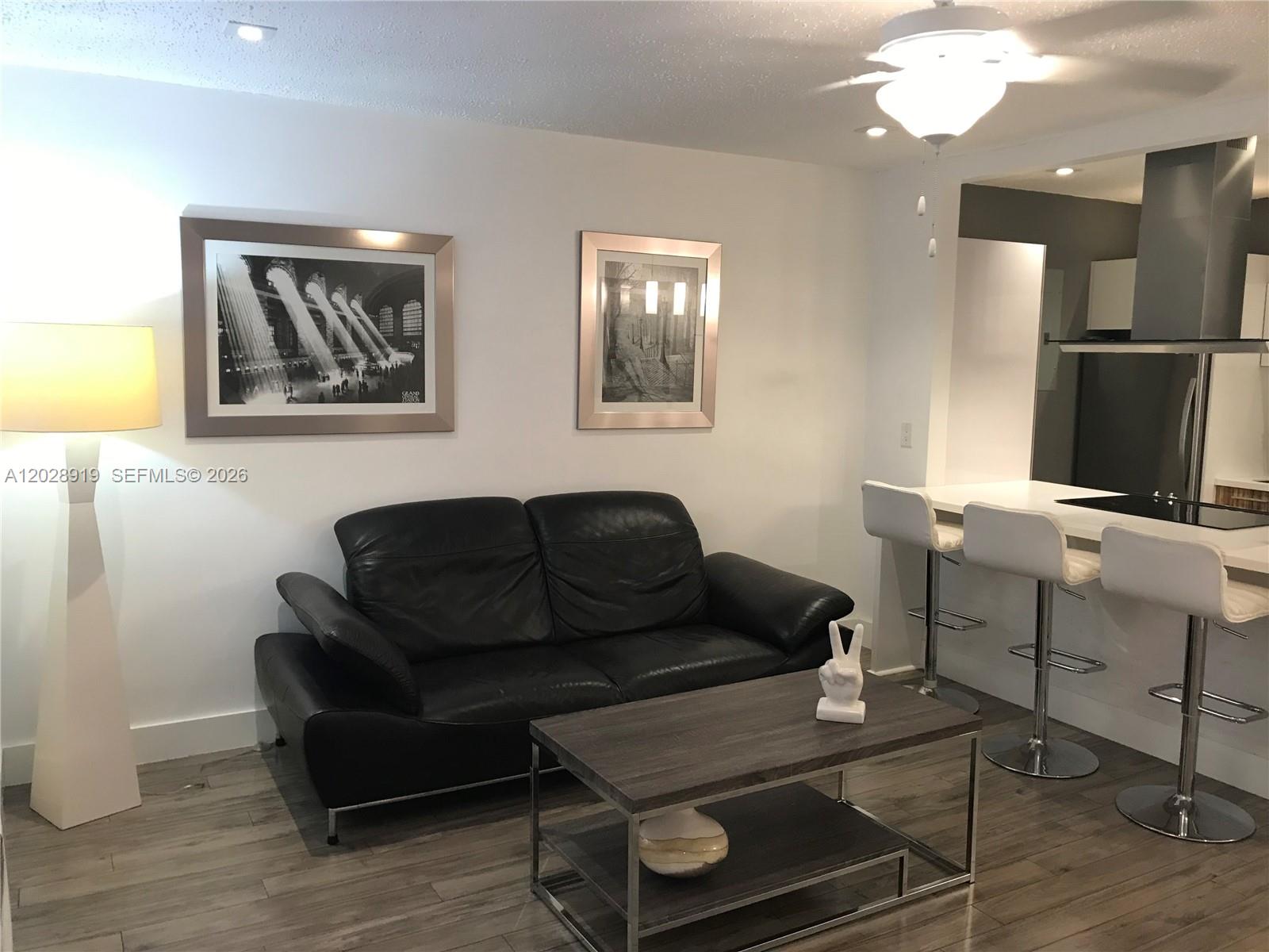 A modern kitchen features a white island with a cooktop, stainless appliances, and bar stools — 2915 Plunkett St # 10D, Hollywood FL 33020, HOLLYWOOD, FL