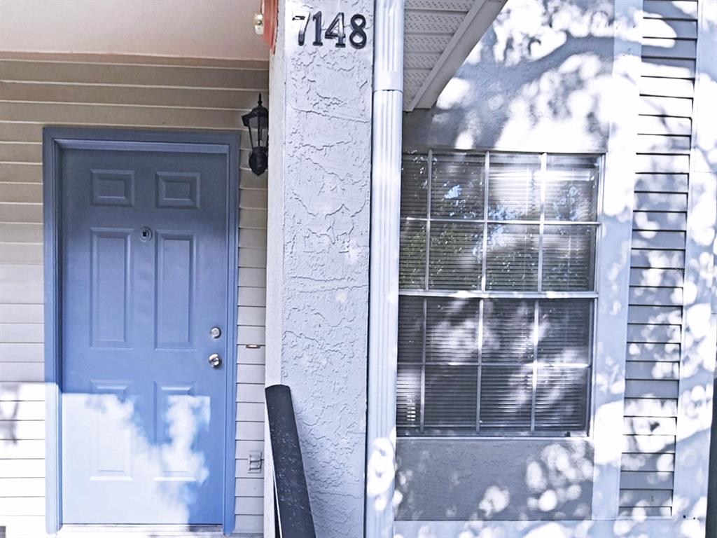 A blue front door sits next to a window on a house with beige siding — 7148 E BANK DRIVE, TAMPA, FL