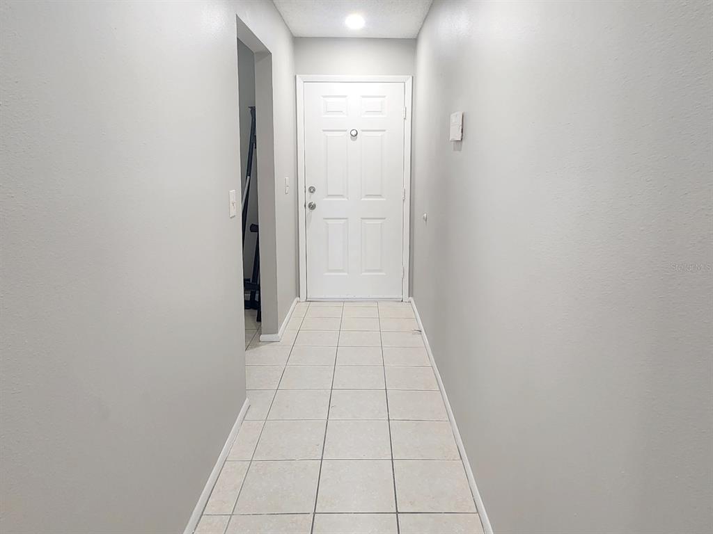 A white front door sits at the end of a hallway with light-colored tile flooring — 7148 E BANK DRIVE, TAMPA, FL