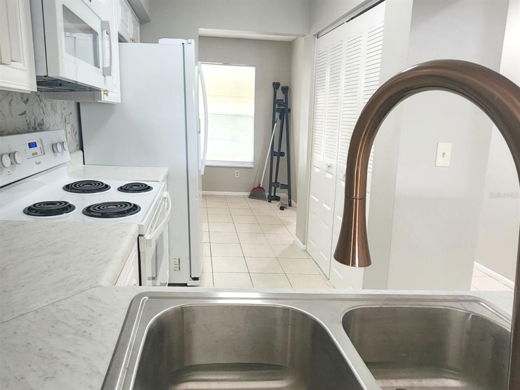 A kitchen features a double-basin sink, white appliances, tiled flooring, and a window — 7148 E BANK DRIVE, TAMPA, FL
