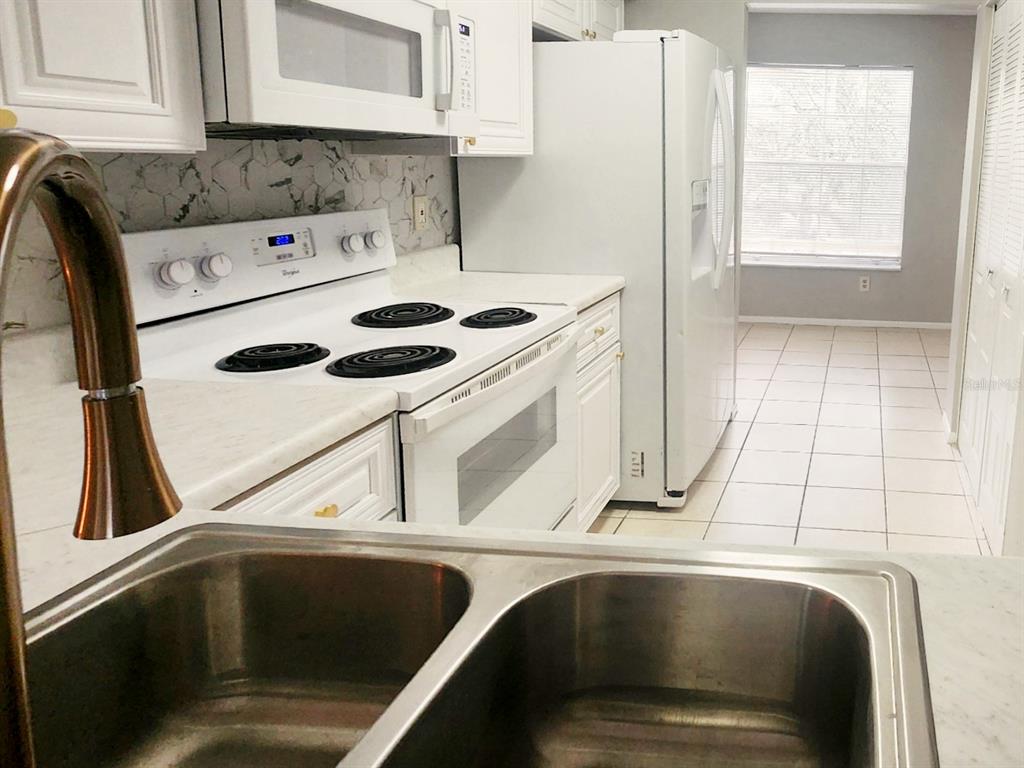 A kitchen features white cabinets, a white electric stove, a refrigerator, and a double-basin sink — 7148 E BANK DRIVE, TAMPA, FL