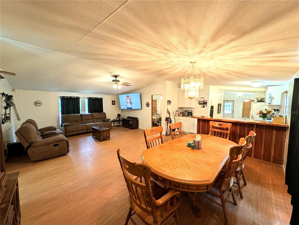 An open-concept living and dining area with wood-look flooring, a chandelier, and a breakfast bar — 23880 NE 121ST LANE, FORT MC COY, FL